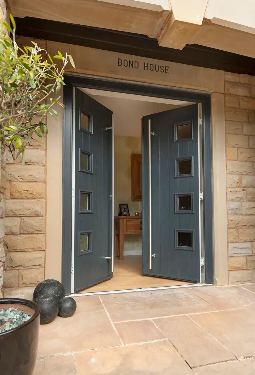 Open grey double doors with square glass lights in a stone-built entrance