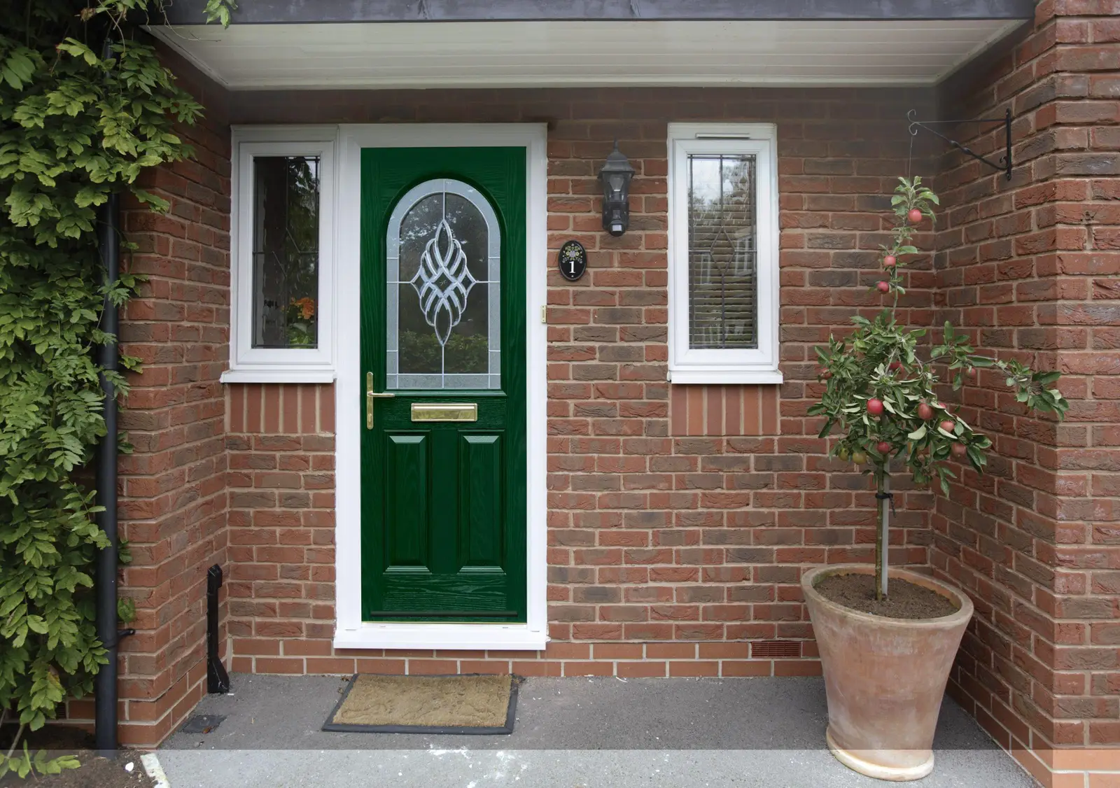 Green composite door with decorative glass and matching side windows in a brick porch